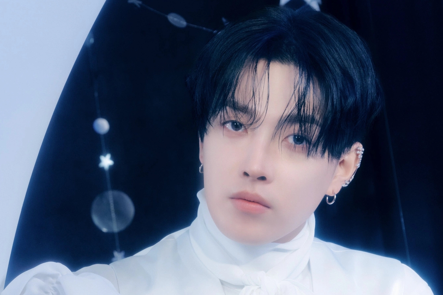 ATEEZ's Hongjoong in a white high-necked shirt against a dark starry backdrop in an official photo