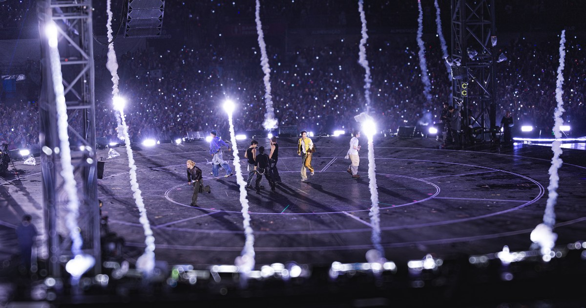 BTS members performing on a circular stage amid pyrotechnic smoke trails in front of a packed stadium crowd in São Paulo