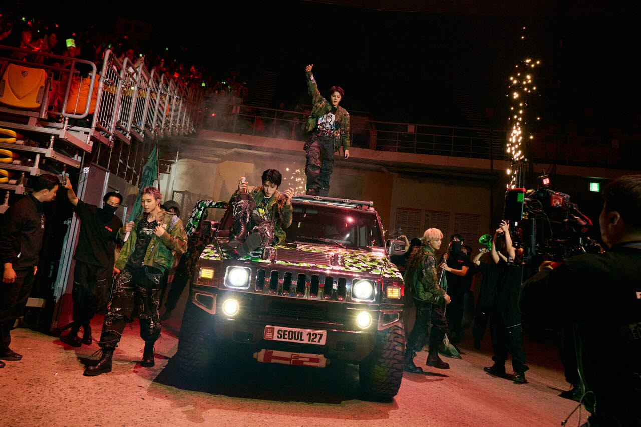 NCT 127 members performing around an SUV with a 'SEOUL 127' plate during THE REDLINE tour