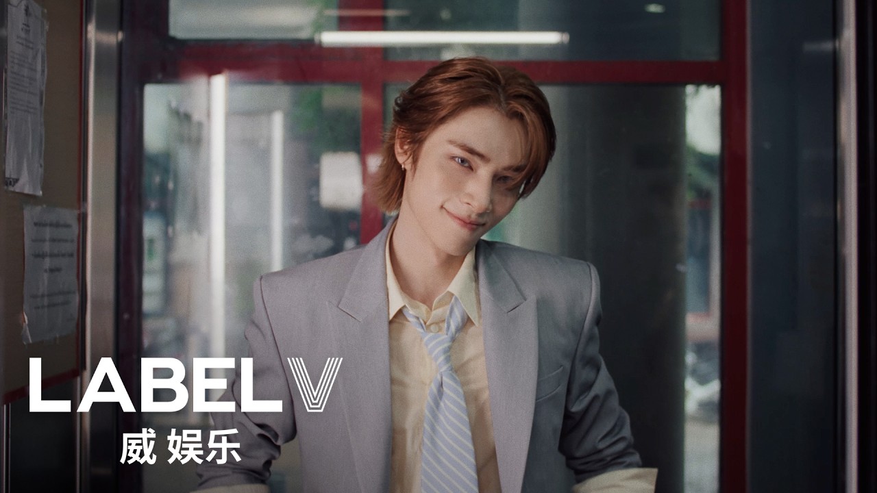 Xiaojun in a grey suit and striped tie in a still from the 'Hey, Somebody (English Ver.)' music video